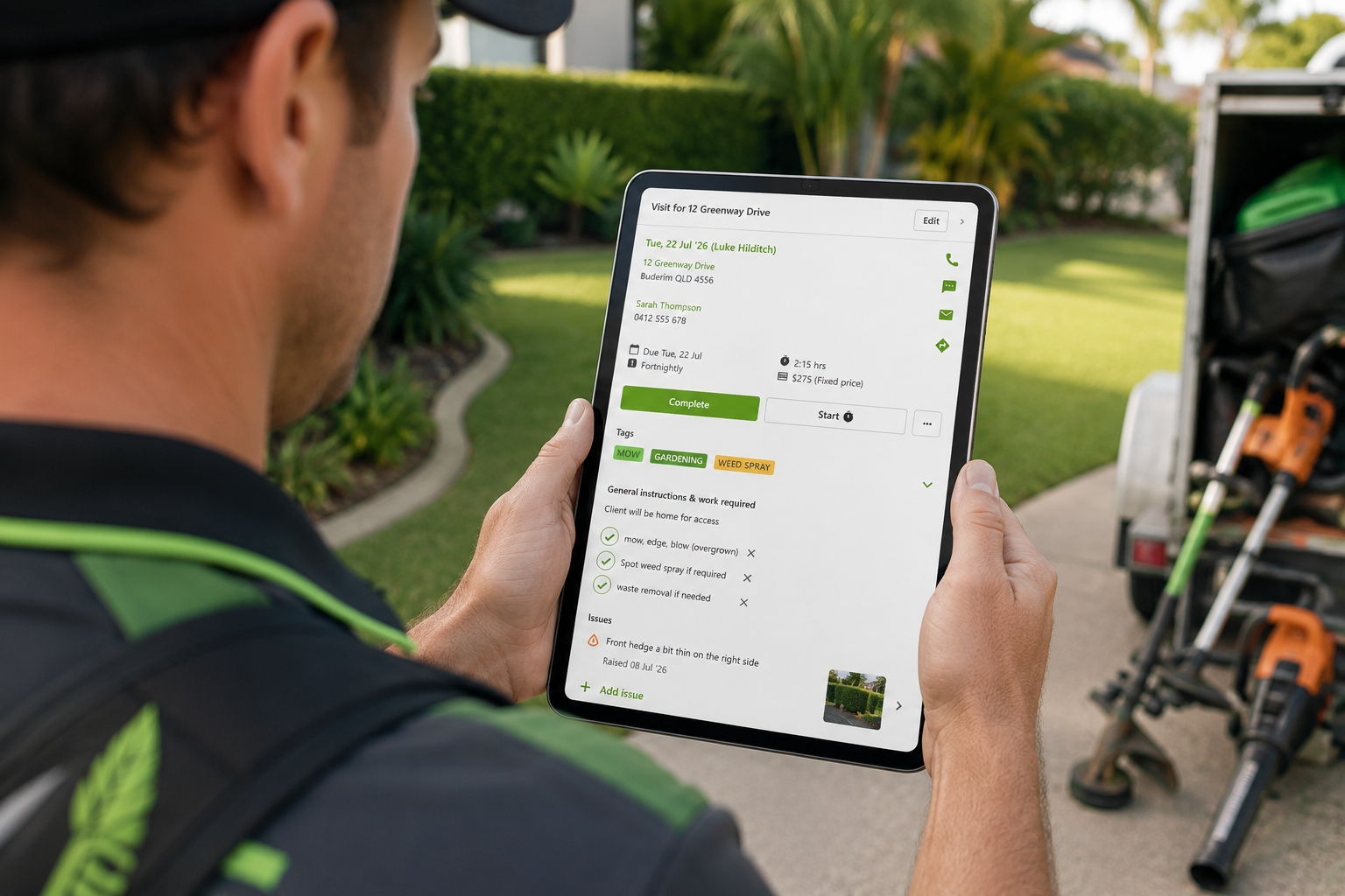Team member reviewing job details on a tablet in front of a freshly mowed lawn