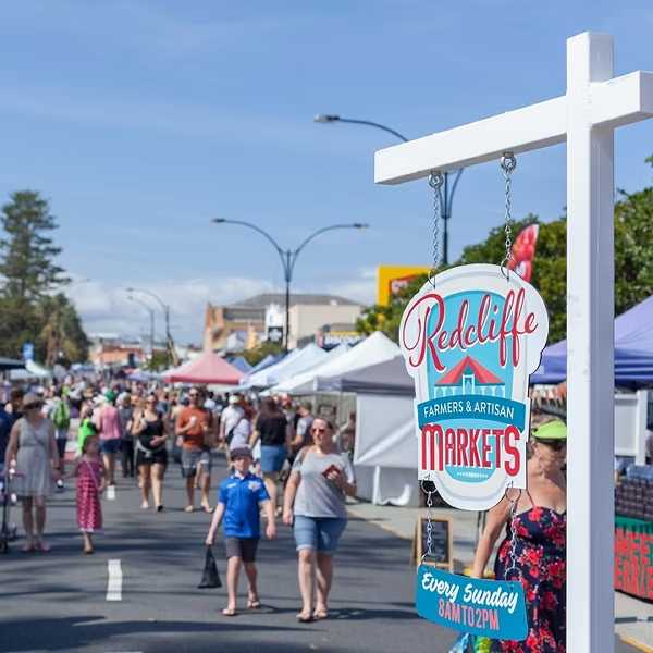 Redcliffe Farmers and Artisan Markets sign along a busy street of market stalls